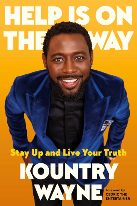 Kountry Wayne holding his book "Help Is on the Way: Stay Up and Live Your Truth" with a confident smile.
