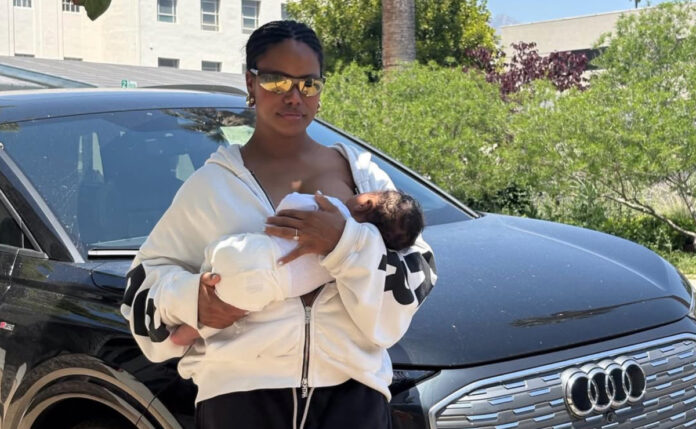 Taylour Paige breastfeeding her newborn son while standing in front of an Audi E Tron after surviving a car accident.