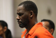 R. Kelly Reportedly Overdoses In Prison As Lawyers Claim Murder Plot, Solitary Abuse R. Kelly in prison clothing with a serious expression during court appearance