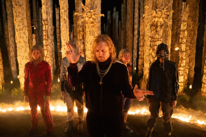 Jack O’Connell stands with a group of survivors surrounded by fire and towering wooden structures in a night scene from “28 Years Later: The Bone Temple.”