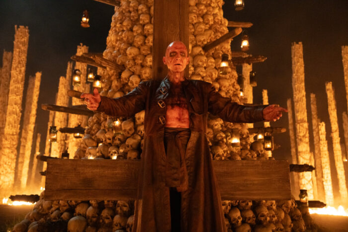 Ralph Fiennes stands before a towering structure made of skulls and candles in a ritual-like setting from “28 Years Later: The Bone Temple.”