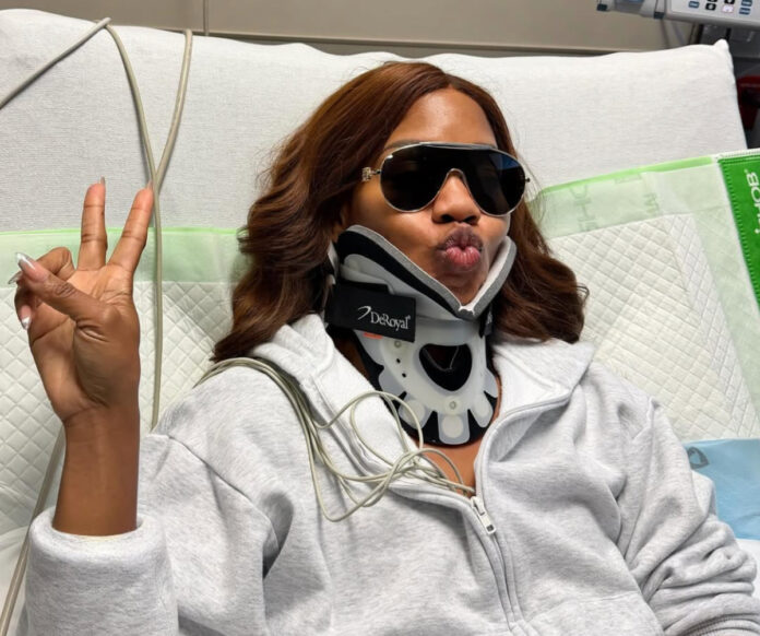 Sarah Jakes Roberts wearing a neck brace in the hospital, sunglasses on, holding up a peace sign after her trampoline accident injury