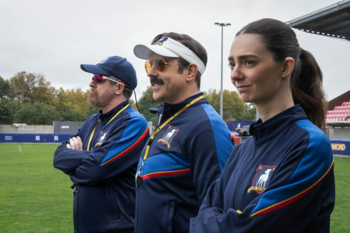 ted-lasso-season-4-coaches-afc-richmond-womens-team Jason Sudeikis as Ted Lasso stands with coaching staff on the field in Ted Lasso Season 4 on Apple TV
