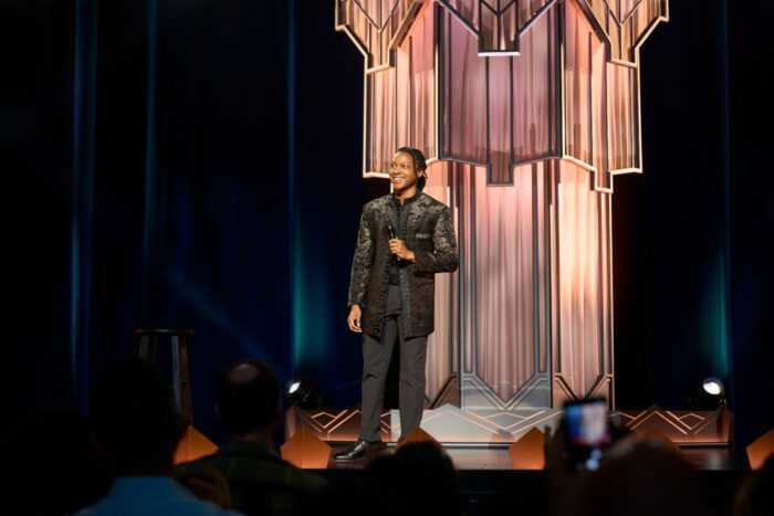 Josh Johnson performing stand-up comedy in Symphony (2026) on stage in front of a live audience